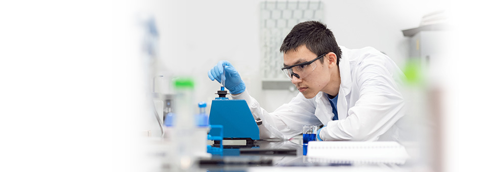 Person in a research lab checking on a equipment wearing a lab coat and PPE.
