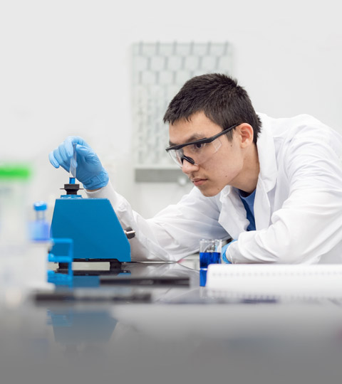Person in a research lab checking on a equipment wearing a lab coat and PPE.