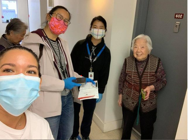 women posing with elderly lady, all wearing masks